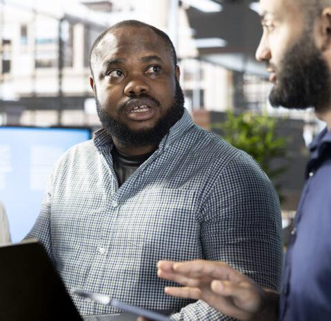 Manager looking at laptop screen with workers, showing them researching key data needed for finding business insights and finishing project task. Management executives analyzing data on notebook